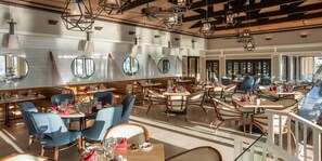 A restaurant with round tables, blue chairs, and a modern interior design.