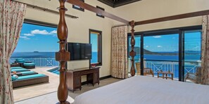 A bedroom with a large bed, a TV, and a view of the sea.