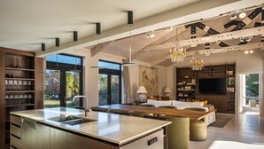 A modern kitchen with a central island, large windows, and a dining area with a chandelier.