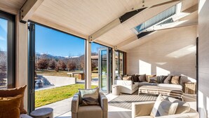A modern living room with a large sliding glass door leading to a balcony, offering a view of a mountainous landscape.