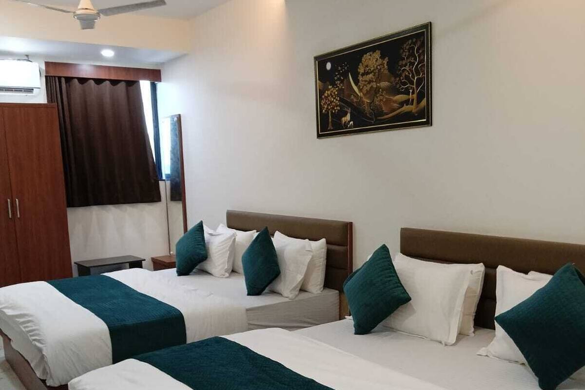 Une chambre d’hôtel avec deux lits, chacun agrémenté de draps blancs et turquoise, un ventilateur de plafond et un tableau au mur.