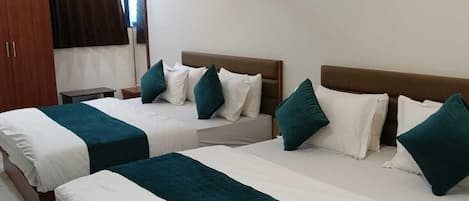 A hotel room with two beds, each with white and teal bedding, a ceiling fan, and a painting on the wall.
