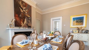 Ein Esszimmer mit langem Tisch, gedeckt für eine Mahlzeit, einem Kamin und einem großen Gemälde an der Wand.
