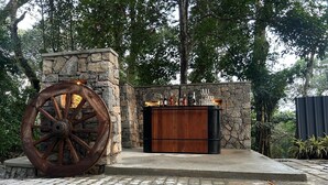 A rustic outdoor bar area with a stone wall and a large wooden wheel. - Hillscape Resort (Madikeri)
