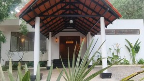 A modern building with a covered entrance, large windows, and a well-maintained garden with various plants. - Hillscape Resort (Madikeri)