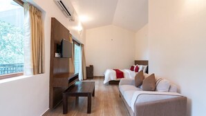 A hotel room with a wooden floor, a bed with white and red bedding, a sofa, a TV mounted on the wall, and a window with curtains. - Hillscape Resort (Madikeri)