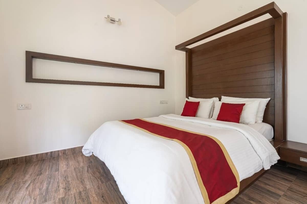 A hotel room with a wooden headboard, a large bed with white bedding and red accents, and a wooden floor.