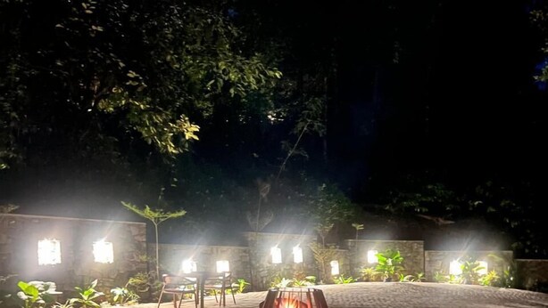 An outdoor seating area with two chairs and a central fire feature, surrounded by stone paving and illuminated by ambient lighting. - Hillscape Resort (Madikeri)
