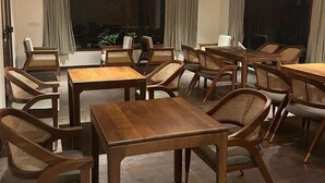 A dining area with wooden tables and chairs, large windows with curtains, and a modern chandelier. - Hillscape Resort (Madikeri)