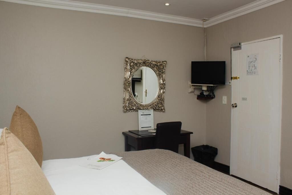 Een hotelkamer met een bed, een bureau met een stoel, een aan de muur bevestigde televisie en een deur met een berichtje erop.