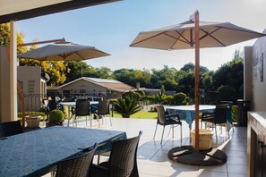 An outdoor patio area with tables and chairs, umbrellas, and a grill. - Oaklands inn and Conference centre  (Randburg)