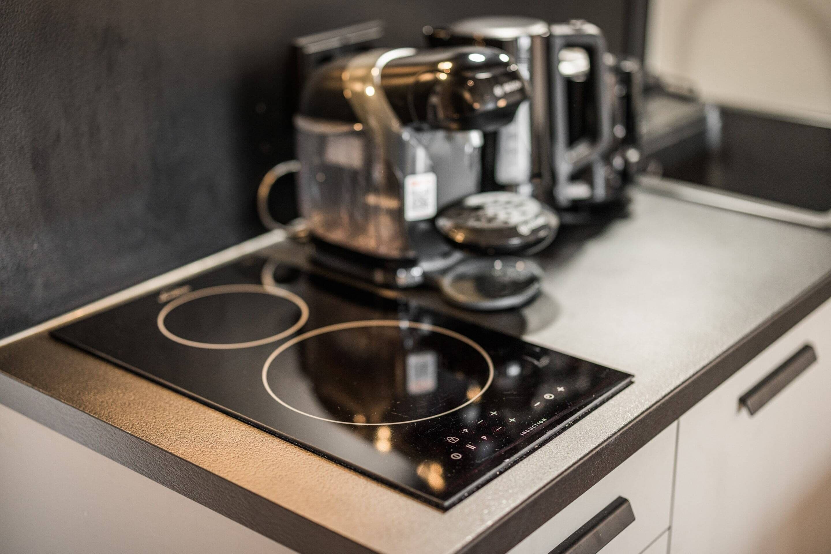 A kitchen with a black induction cooktop and a coffee maker.