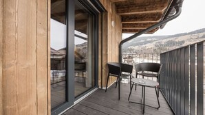 Ein Holzbalkon mit zwei Stühlen und einem Tisch, der auf eine gebirgige Landschaft blickt.