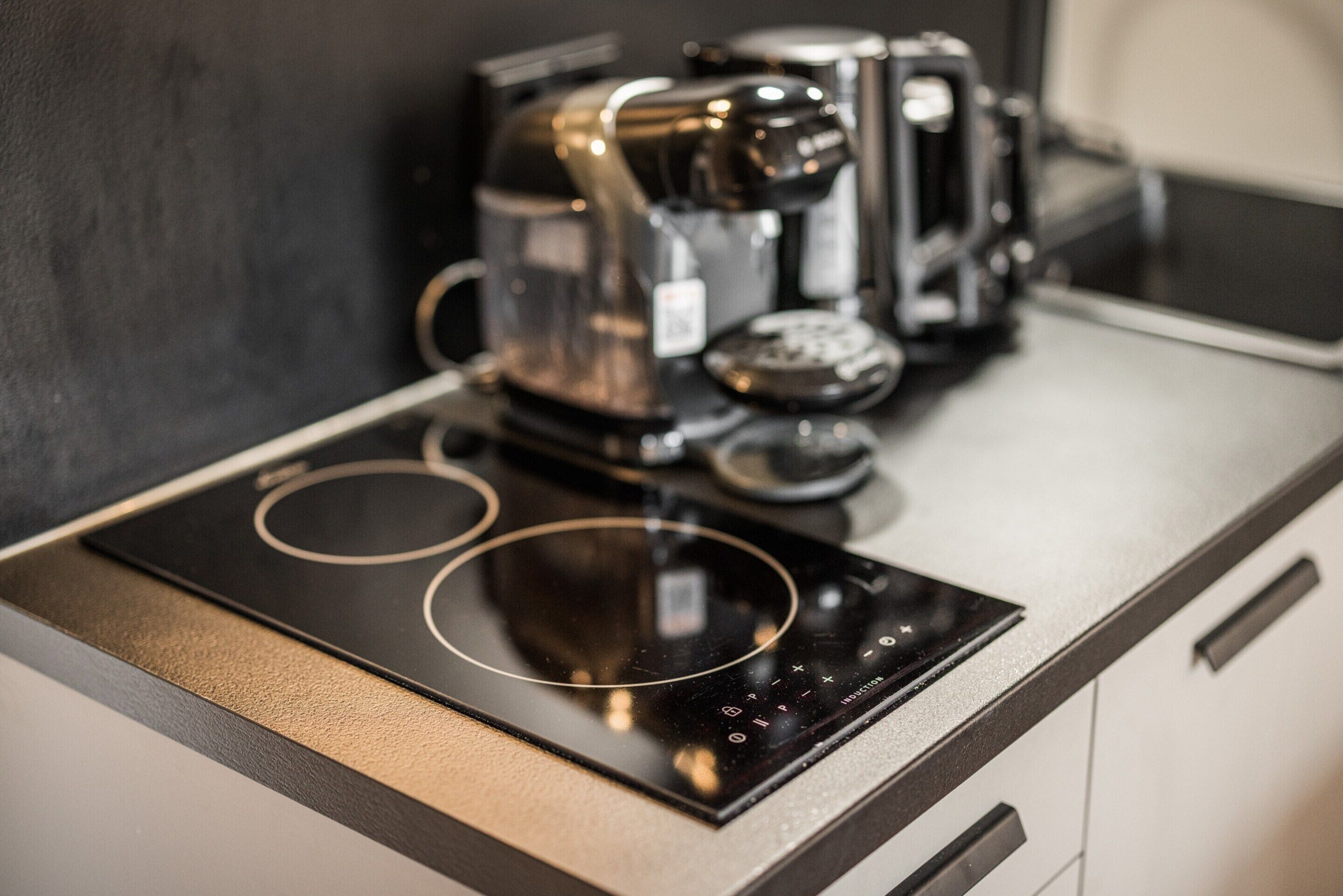 Une cuisine avec une plaque de cuisson à induction noire, une machine à café et une bouilloire posées sur le plan de travail.