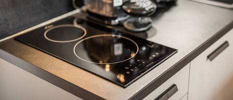 A kitchen with a black induction cooktop, a coffee maker, and a kettle on a countertop.