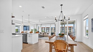 A spacious kitchen with a central island, a dining area with wicker chairs, and large windows offering views of the city.