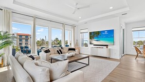 A spacious living room with a large TV, comfortable seating, and a view of the beach.