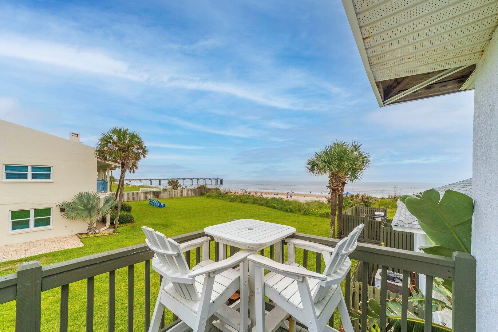 Un balcon avec une table et des chaises donnant sur une plage et une jetée.