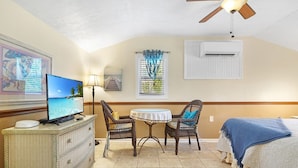 A room with a television, wicker furniture, a ceiling fan, and a bed with a blue blanket.