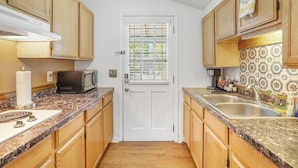A compact kitchen with wooden cabinets, a white door, and a tiled backsplash.