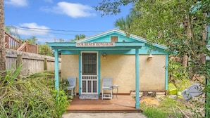 A small beach bungalow with a porch, two chairs, and a small table.