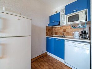 Una cocina compacta con un refrigerador blanco, gabinetes azules, un microondas y una cafetera.