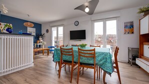 Un comedor con una mesa preparada para cuatro personas, un televisor montado en la pared y un amplio ventanal con vistas al exterior.