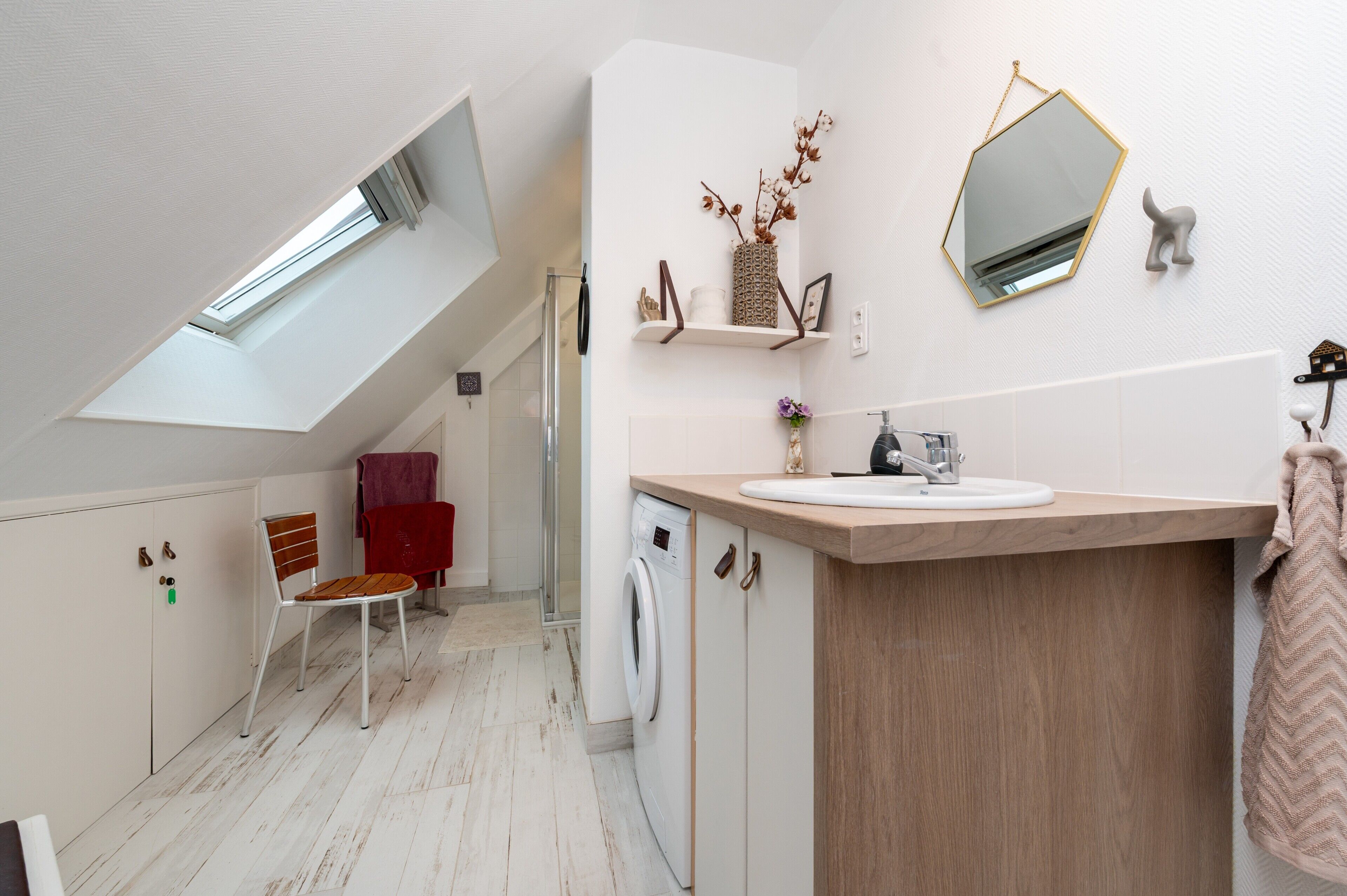 Ein modernes Badezimmer mit Dachfenster, einer Waschmaschine, einem Waschbecken und einem Stuhl.