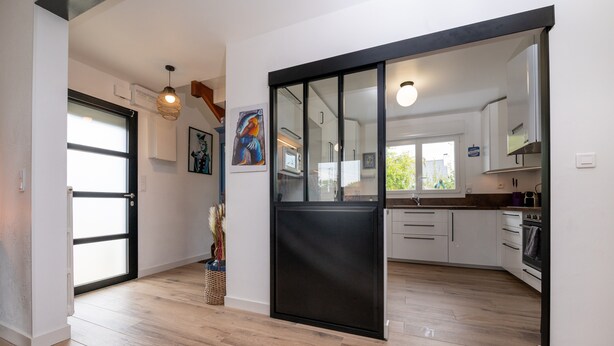Una cocina moderna con armarios blancos, un refrigerador negro y piso de madera.