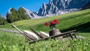 Un espacio de estar al aire libre rústico con un banco de madera, un cojín blanco y un barril de madera con flores rojas.
