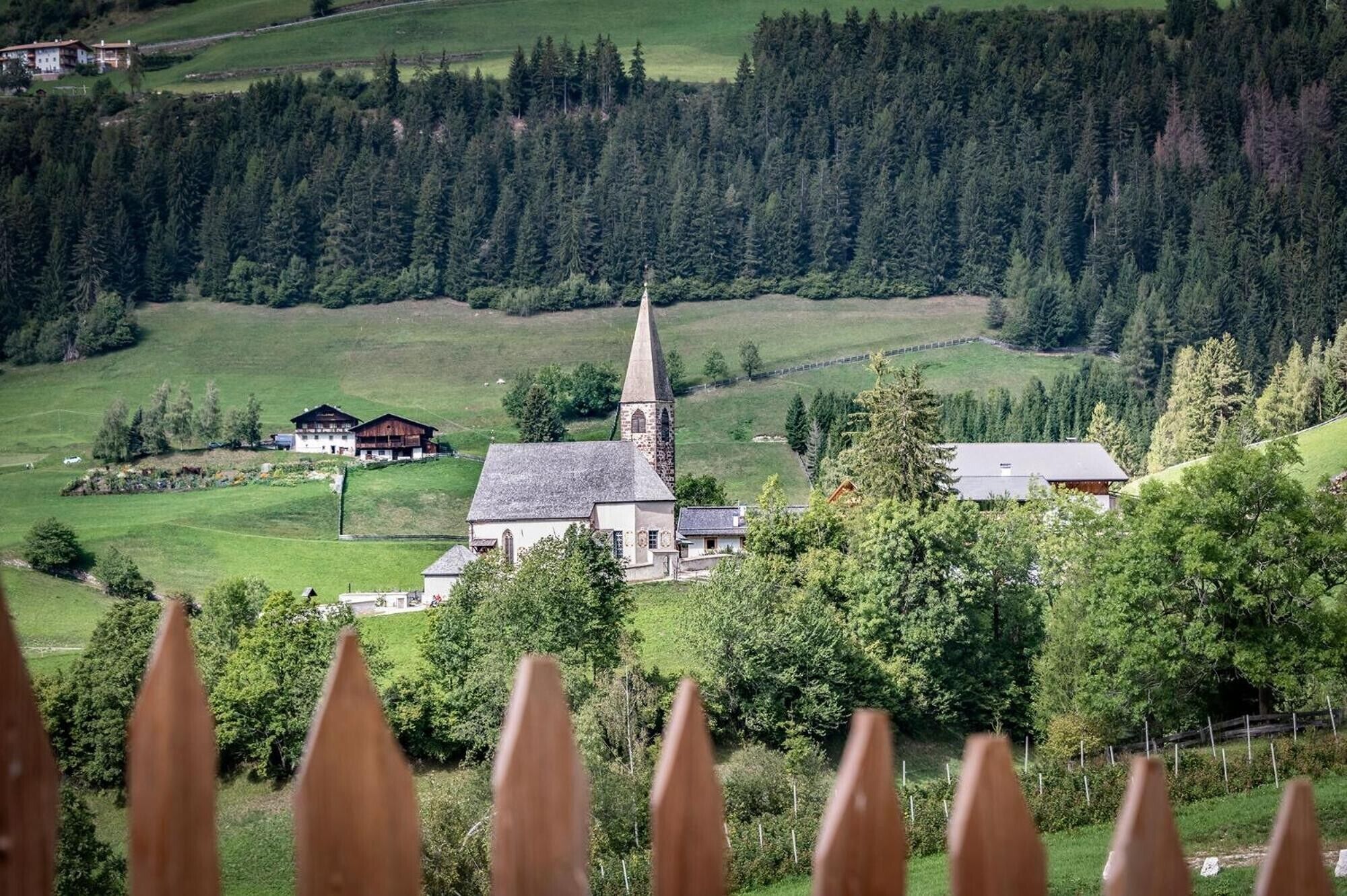 Een kerk met een hoge kerktoren, omgeven door groene velden en bomen.
