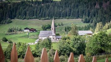 Een kerk met een hoge kerktoren, omgeven door groene velden en bomen.