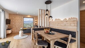 Un interior moderno con una zona de comedor de madera, un sofá y un televisor montado en la pared.