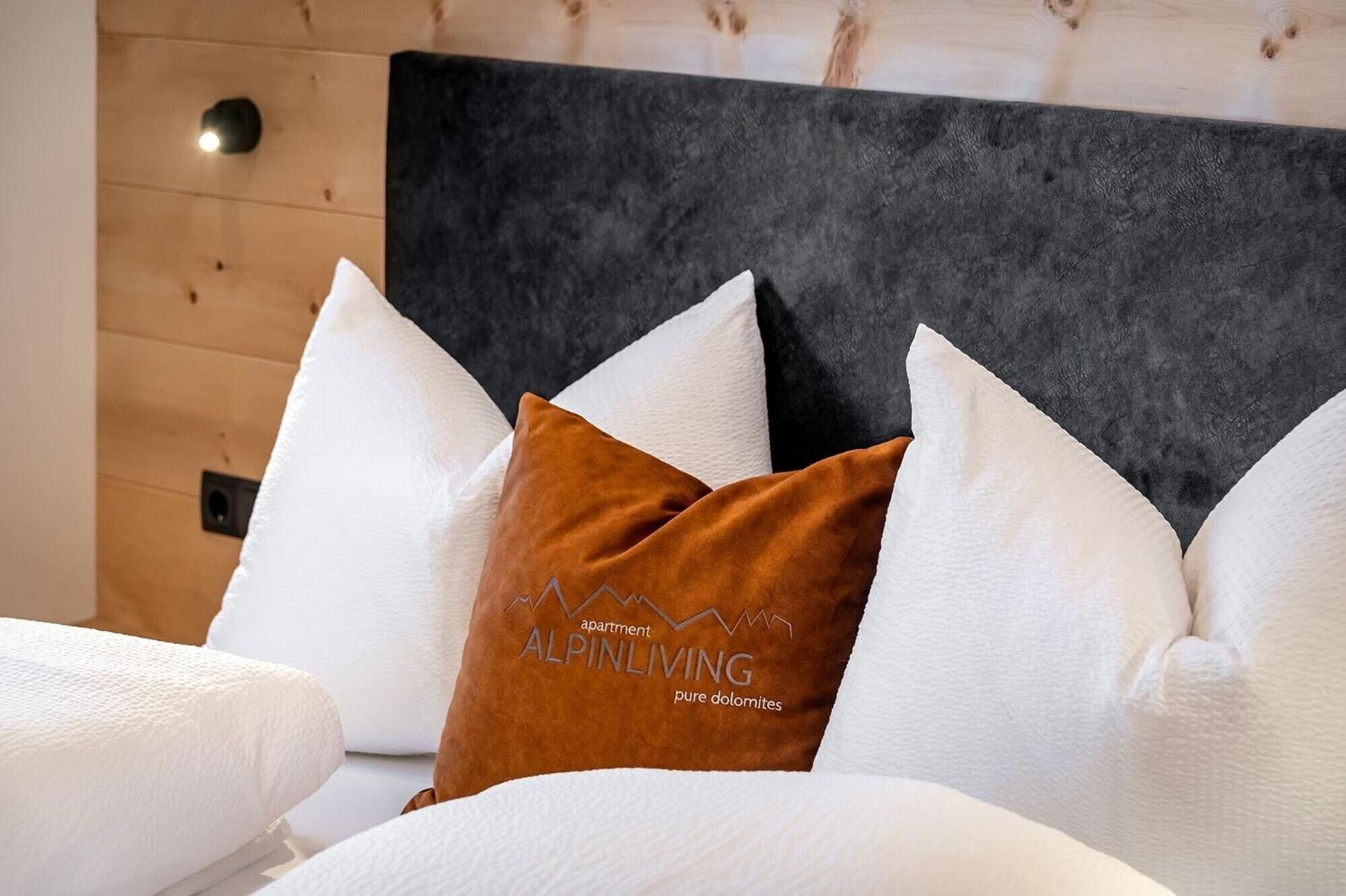 Un lit avec une literie blanche et un oreiller marron orné du texte « ALPINLIVING ».