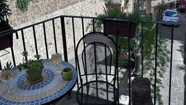 Un balcón con una mesa y sillas de cerámica, con vistas a una calle con edificios y coches.
