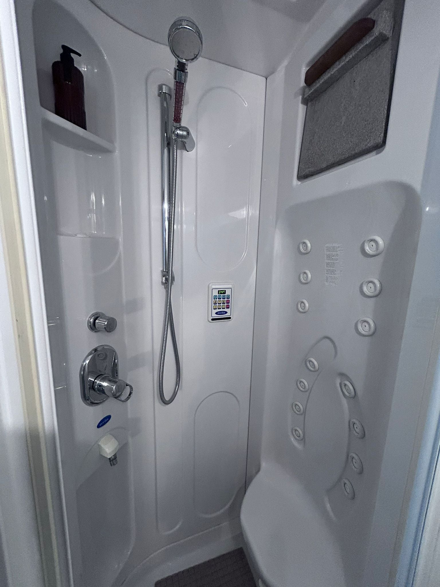 A small, white, walk-in shower with a handheld showerhead, a handheld shower attachment, and a control panel with buttons and a digital display.