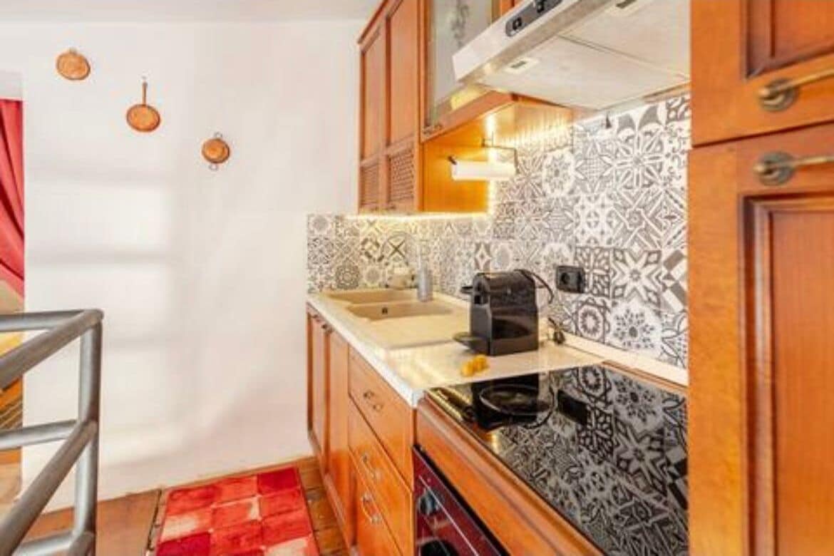 A compact kitchen with patterned tiles, wooden cabinets, and a stainless steel sink.