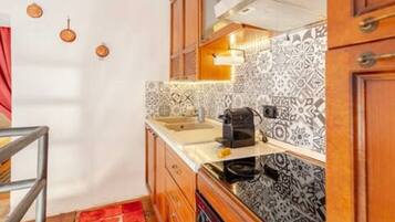 A compact kitchen with patterned tiles, wooden cabinets, and a stainless steel sink.