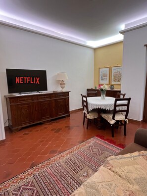 A living room with a television displaying 'NETFLIX,' a dining table with chairs, a patterned rug, and a sofa. - 10 minutes from St. Peter's, Entire apartment in quiet and peaceful area. (Roma)