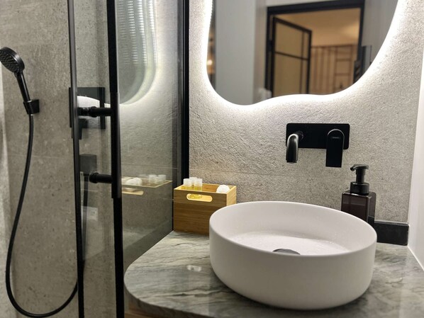 A modern bathroom with a glass-enclosed shower, a white sink, and a mirror reflecting the room.