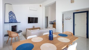 Una sala de estar moderna con una mesa de comedor de madera, sofás blancos y una chimenea.