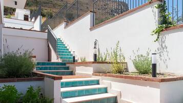 Una scala con gradini blu che conduce a un balcone, circondata da muri bianchi e vegetazione.