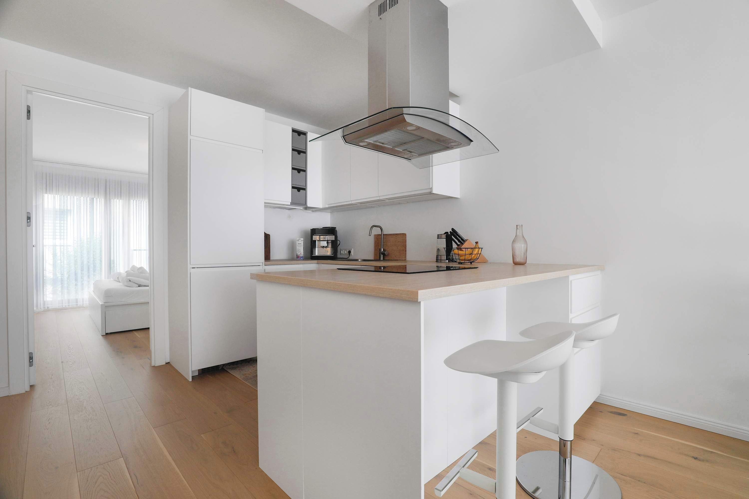 Une cuisine moderne avec des meubles blancs, un îlot central doté de tabourets et une cuisinière encastrée.
