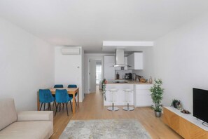 Un salon moderne comprenant un canapé, une table à manger avec des chaises, un coin cuisine avec une cuisinière et un téléviseur.