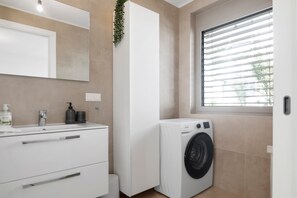 A modern bathroom with a white sink, mirror, and a built-in washing machine.