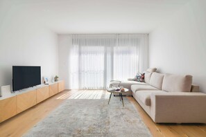 A modern living room with a flat-screen TV, a beige sofa, a small round coffee table, and a wooden cabinet.