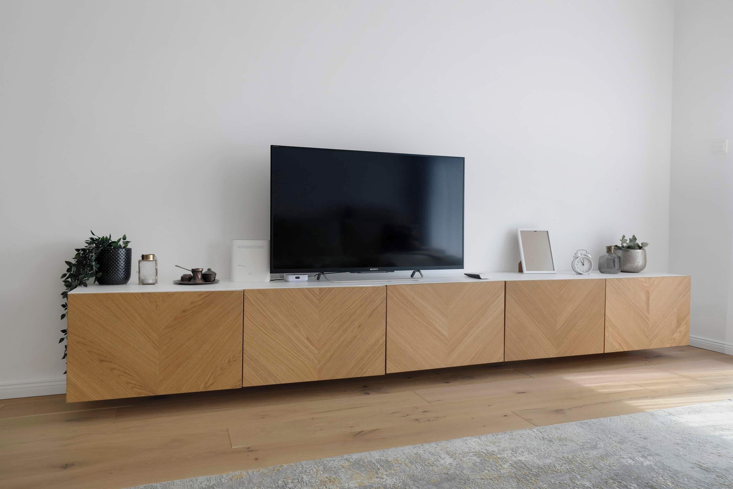 Una sala de estar moderna con un televisor de pantalla plana sobre un mueble de madera, una planta pequeña, un cuadro enmarcado y un reloj.