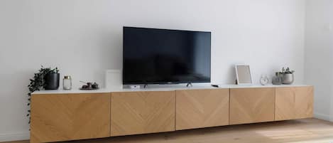Ett modernt vardagsrum med en platt-TV placerad på en träkonsol, en liten växt, en inramad tavla och en klocka.