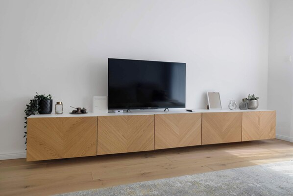 Un salon moderne avec un téléviseur à écran plat posé sur une console en bois, une petite plante, un tableau encadré et une horloge.