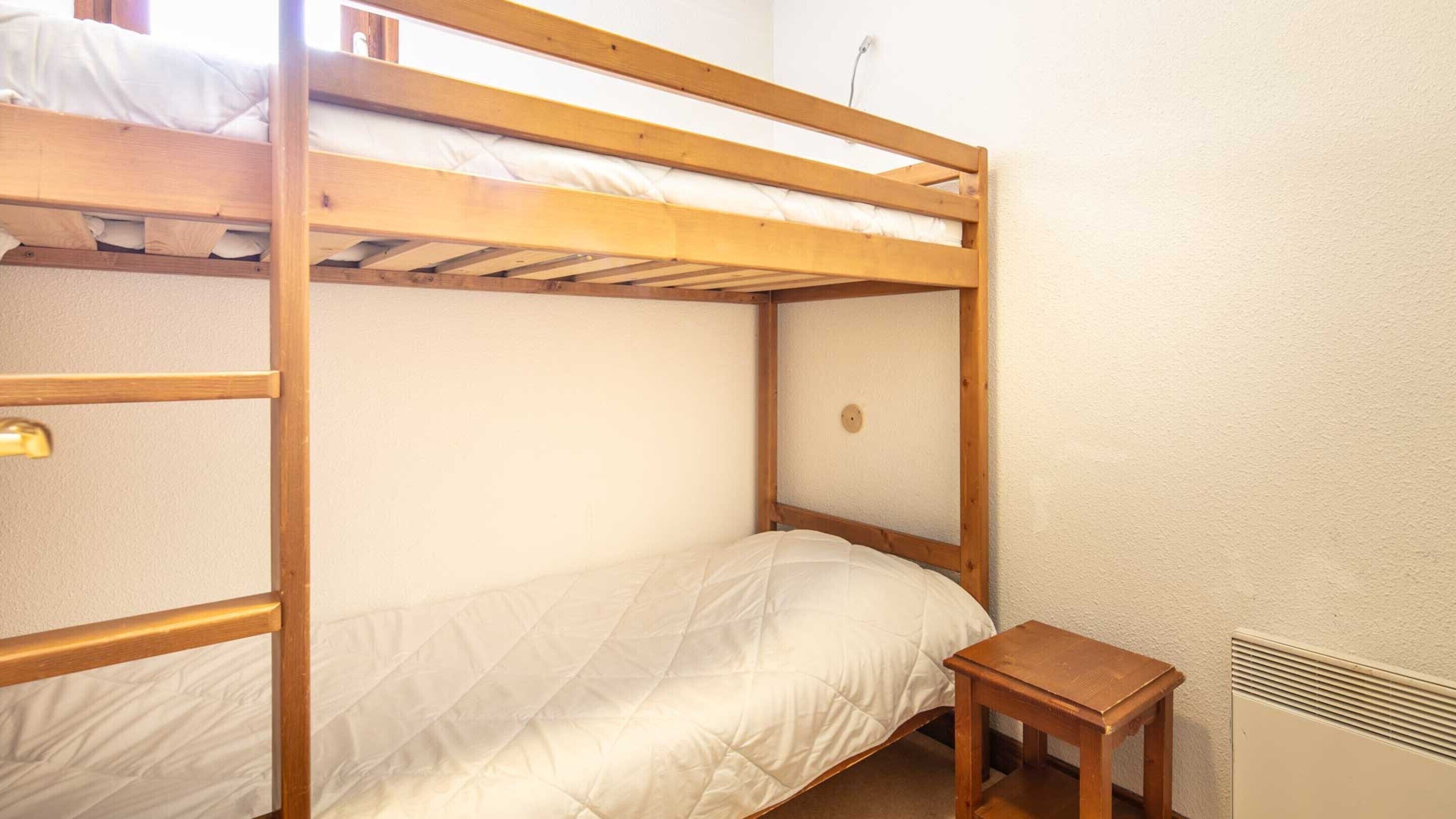 Een slaapkamer met een stapelbed en een klein houten tafeltje er naast.